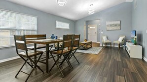 A dining area with a wooden table and chairs, a small side table with a vase, and a television on a stand. - Huge backyard and new reconstruction  (St. Augustine)