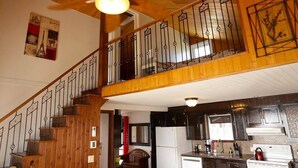 A wooden interior with a staircase, kitchen area, and a ceiling fan.