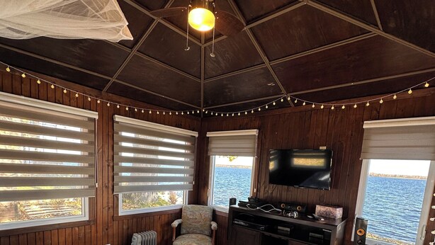 A cabin with a bed, a chair, a TV, and a view of the water.