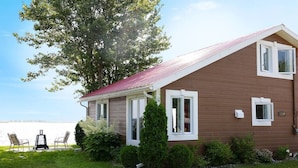 A two-story house with a red roof, white trim, and a number 3508 on the side. There is a lawn with a bench and a tree in the front yard.