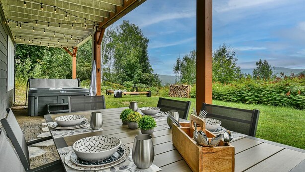 Ett utomhusområde med plats för måltider, en pergola, en grill och en vacker utsikt över träd och berg.