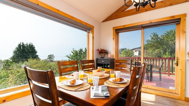 Zona pranzo con tavolo apparecchiato per la colazione, ampie finestre e vista sull'esterno.