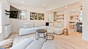 A modern living room with a sectional sofa, a small table, and a kitchen area with bar stools. - Hôtel à la maison - Ô coeur d'Eastman avec spa ! (Eastman)