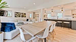 A modern kitchen with white cabinetry, a wooden dining table, and bar stools. - Hôtel à la maison - Ô coeur d'Eastman avec spa ! (Eastman)