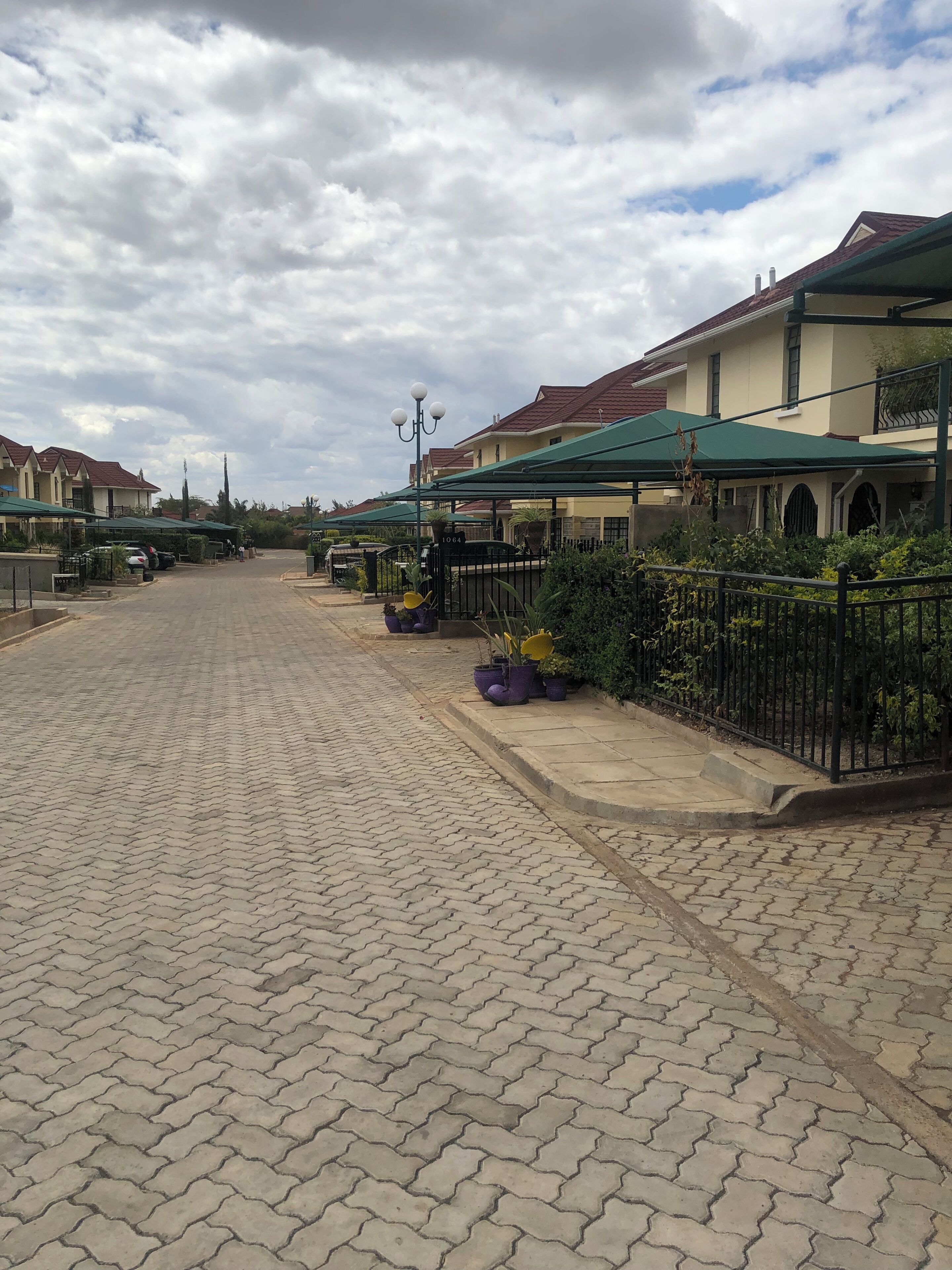 A paved walkway with a row of houses on one side and a covered outdoor seating area on the other.