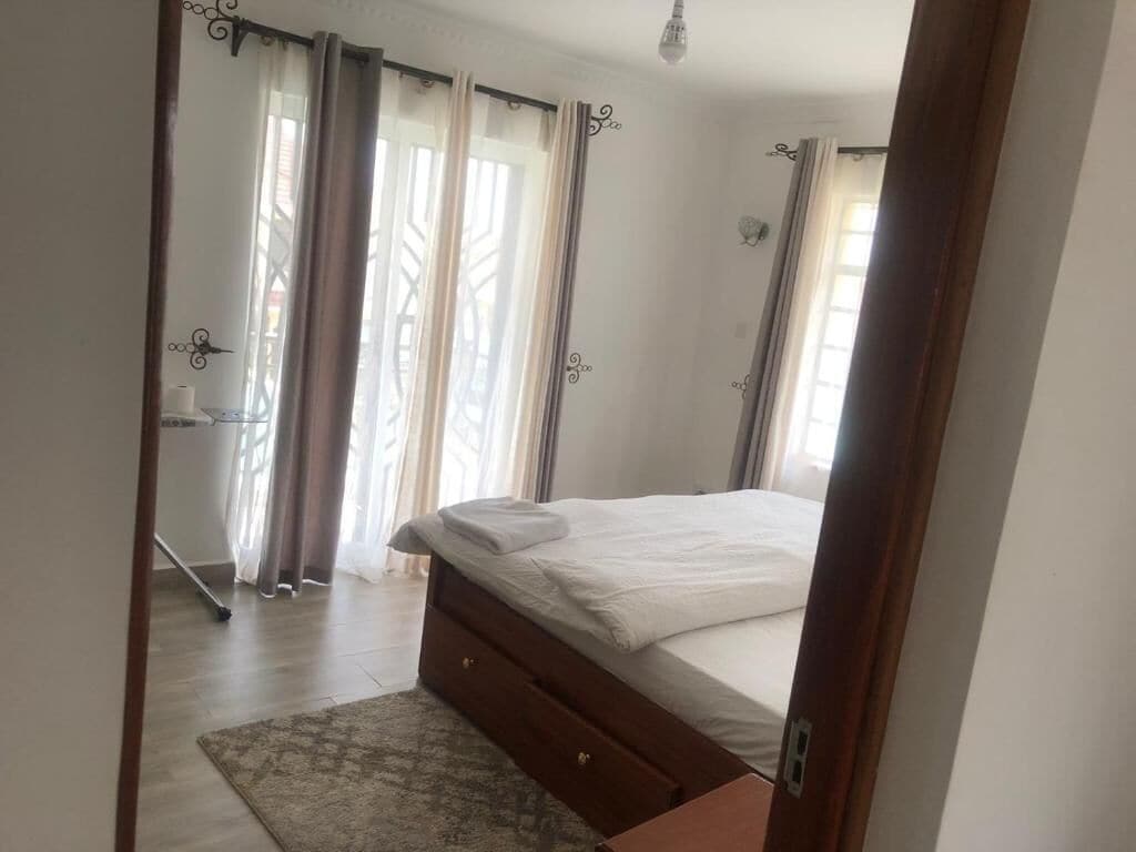 A bedroom with a bed, curtains, a wooden floor, and a small rug.