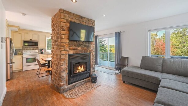 Una sala de estar moderna con chimenea de piedra, un sofá gris y una zona de comedor con piso de madera.