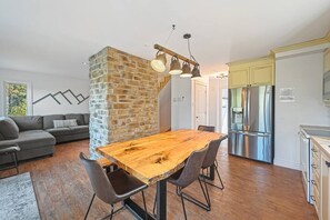 A modern kitchen with a large wooden table, a stone accent wall, and stainless steel appliances.