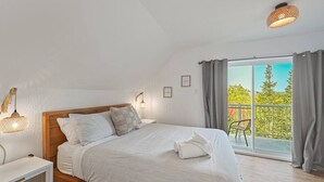 Un dormitorio con una cama grande, una mesita de noche, una lámpara y vistas al exterior a través de una puerta corrediza de vidrio.