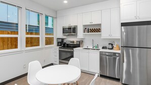 A modern kitchen with white cabinets, stainless steel appliances, and a dining area with white chairs. - Skywalker Rebel Base (Seattle)