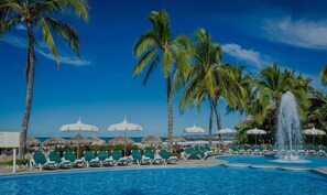 Relax by the pool surrounded by palm trees and lounge chairs, with umbrellas and a soothing water feature nearby.