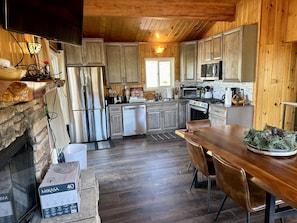 A modern kitchen with wooden cabinets, stainless steel appliances, and a stone fireplace. - cabin with a view (Big Bear Lake)