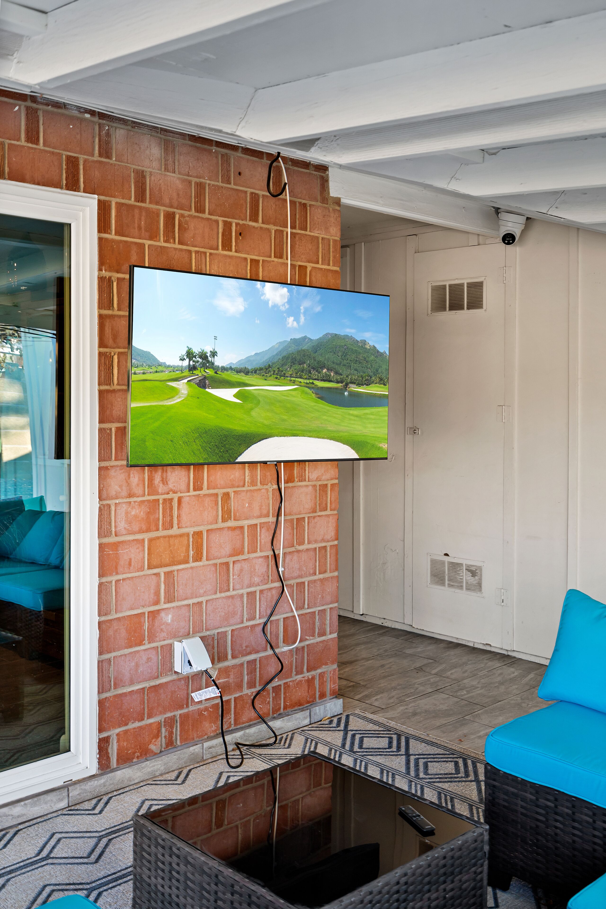 A room with a television mounted on a brick wall, a blue chair, and a patterned rug.