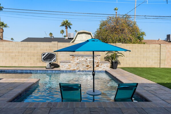 A swimming pool with two green chairs and a blue umbrella, surrounded by a brick wall and a palm tree. - Old Town Scottsdale Desert Oasis- FREE heated pool (Scottsdale)