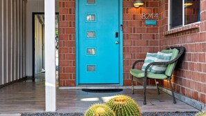 Une porte bleue, une chaise verte et des cactus dans une cour.