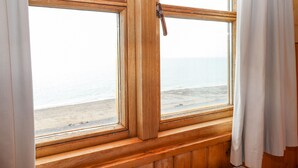 Una ventana con marco de madera y cortinas blancas, con vista a una playa.