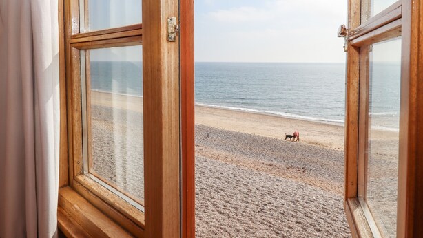 Vista de una playa a través de una ventana abierta con marco de madera.