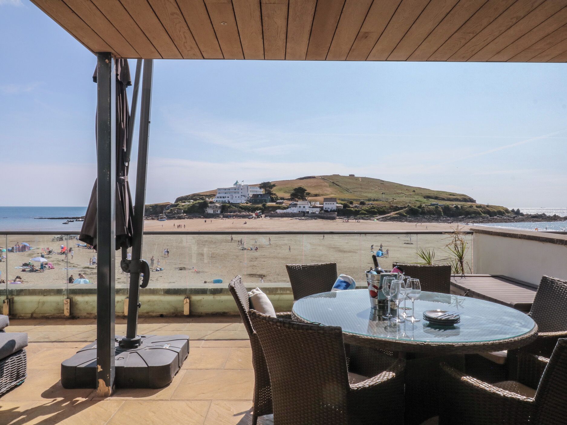 Une terrasse avec une table et des chaises donnant sur une plage et une colline.
