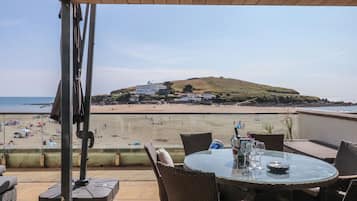 Une terrasse avec une table et des chaises donnant sur une plage et une colline.