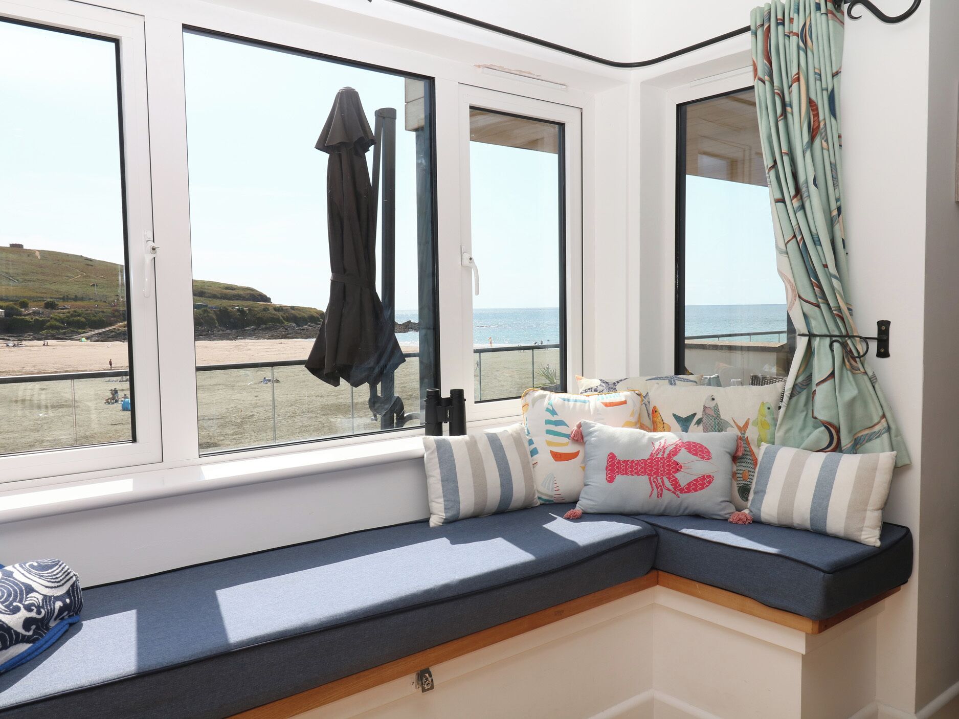 Asiento junto a la ventana con vista a la playa, un par de binoculares y una cortina estampada.