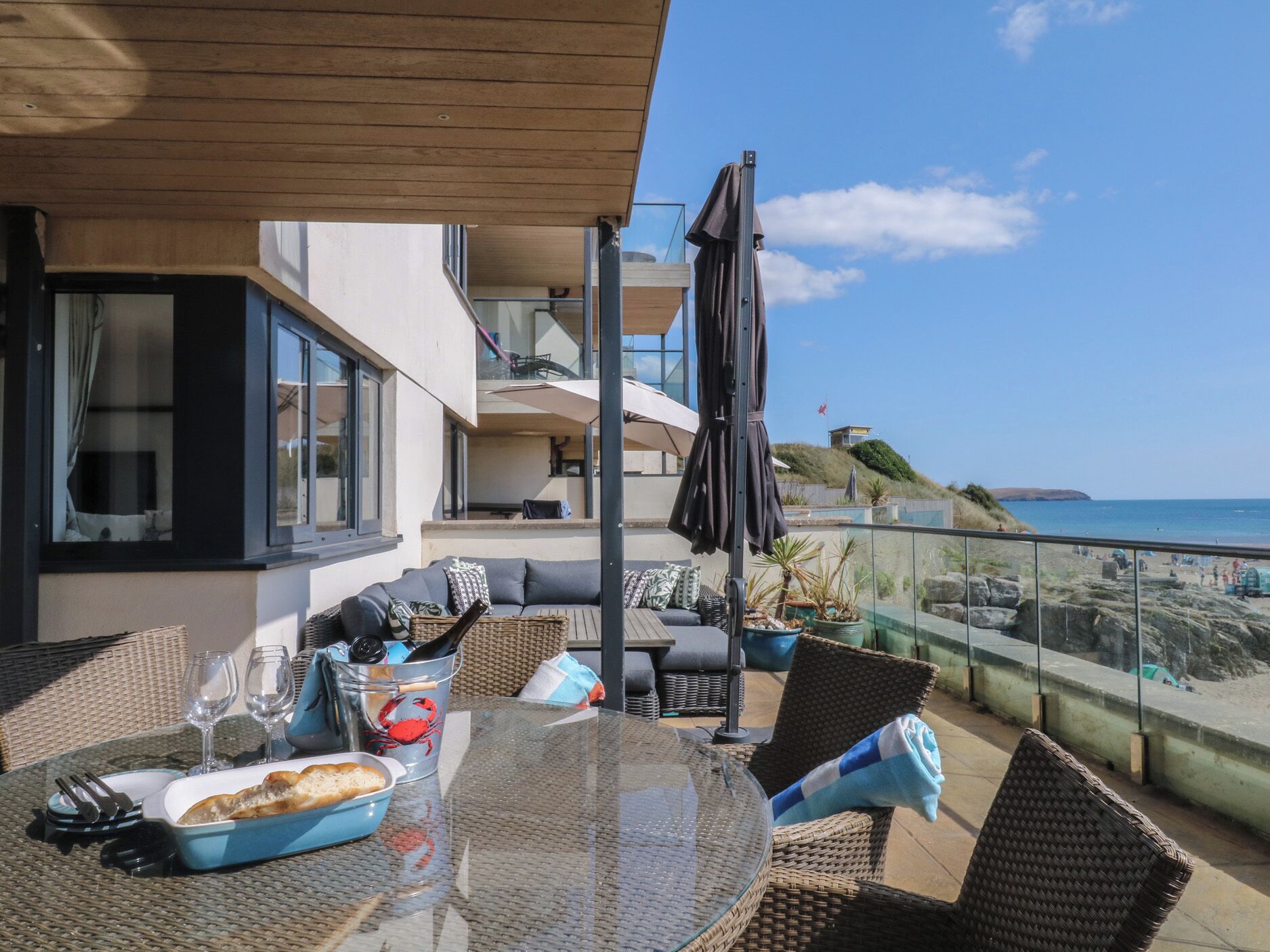 Un balcón con mesa lista para comer, asientos exteriores y vista al mar.