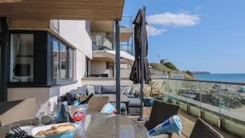 Un balcón con mesa lista para comer, asientos exteriores y vista al mar.
