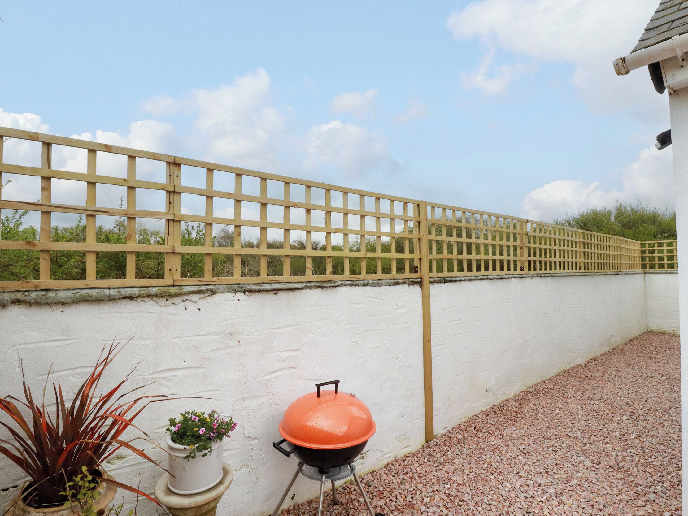 A patio area with a white wall, a wooden fence, and a barbecue grill.