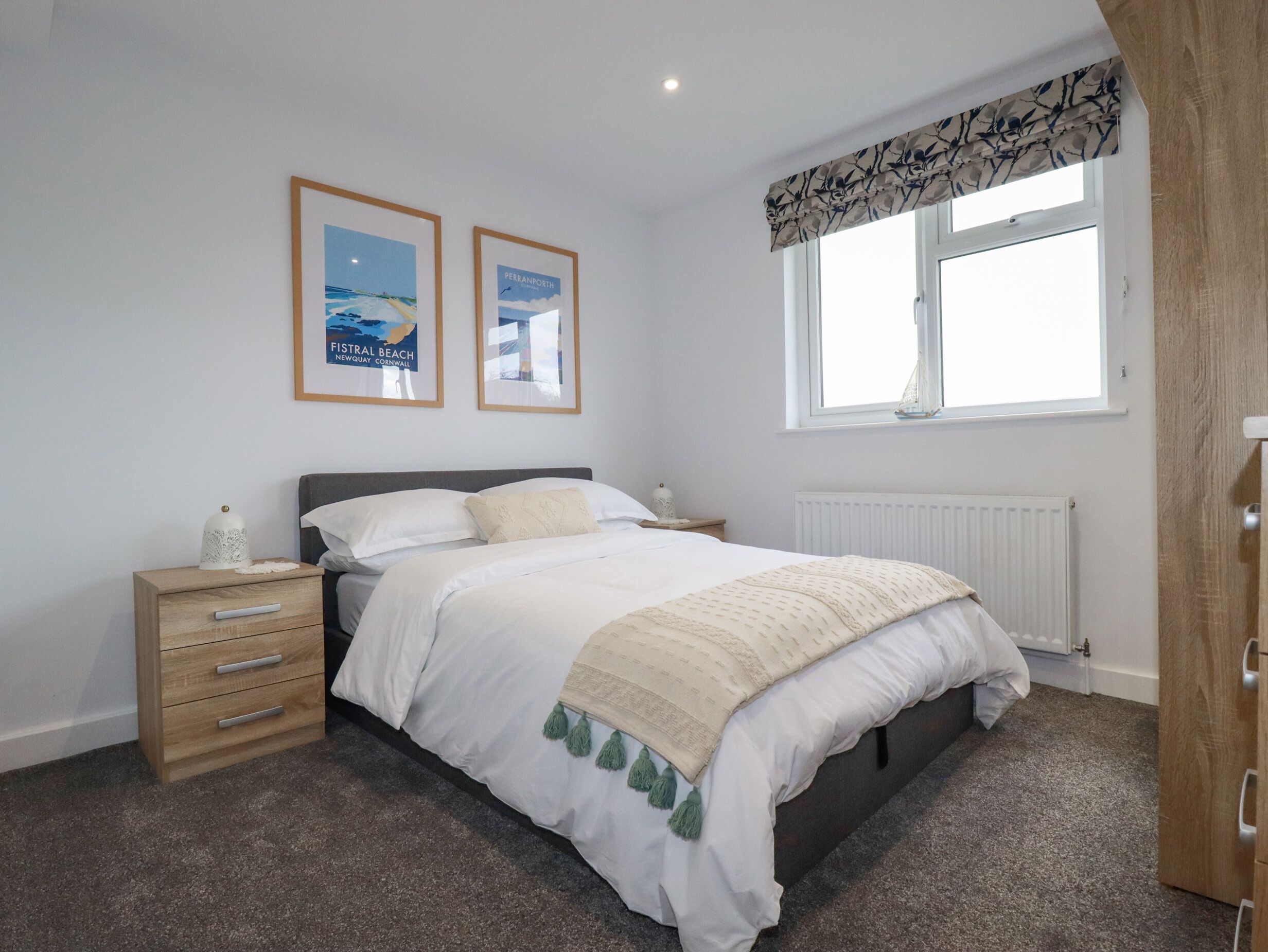 A bedroom with a bed, a nightstand, a dresser, a window with a view, and two framed pictures on the wall.