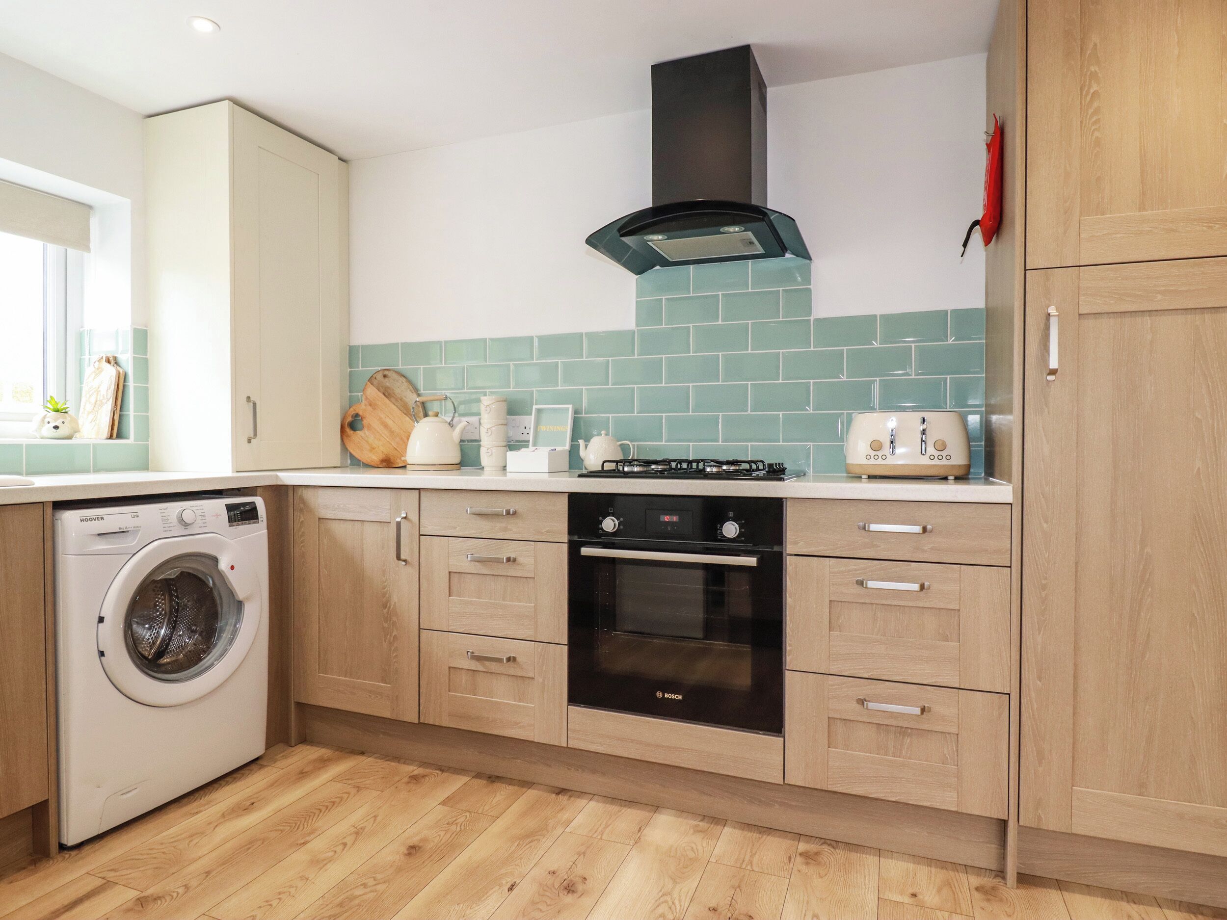 A compact kitchen with a washing machine, a Bosch oven, and a toaster.