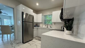 A modern kitchen with white cabinets, a stainless steel refrigerator, and a marble-tiled floor.