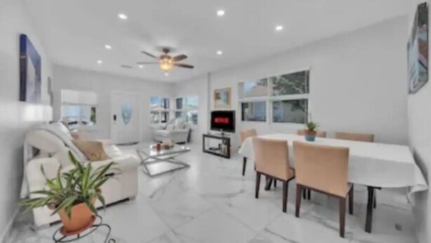 A modern living room with a white sofa, a dining table with chairs, a coffee table, and a ceiling fan.