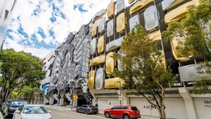 Un edificio con una facciata originale caratterizzata da ampi motivi bianchi astratti e un cartello parcheggio ben visibile.