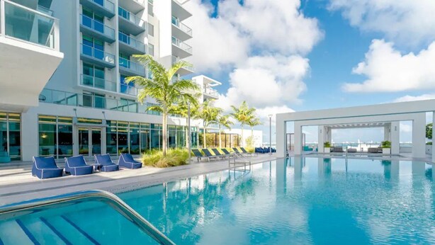 Un hotel moderno con una grande piscina esterna, lettini e palme.