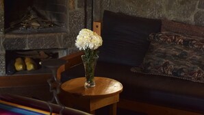 A cozy room with a stone fireplace, a wooden bench, and a table with a colorful tablecloth. - Casa Qatzij - Guest House (San Lucas Toliman)