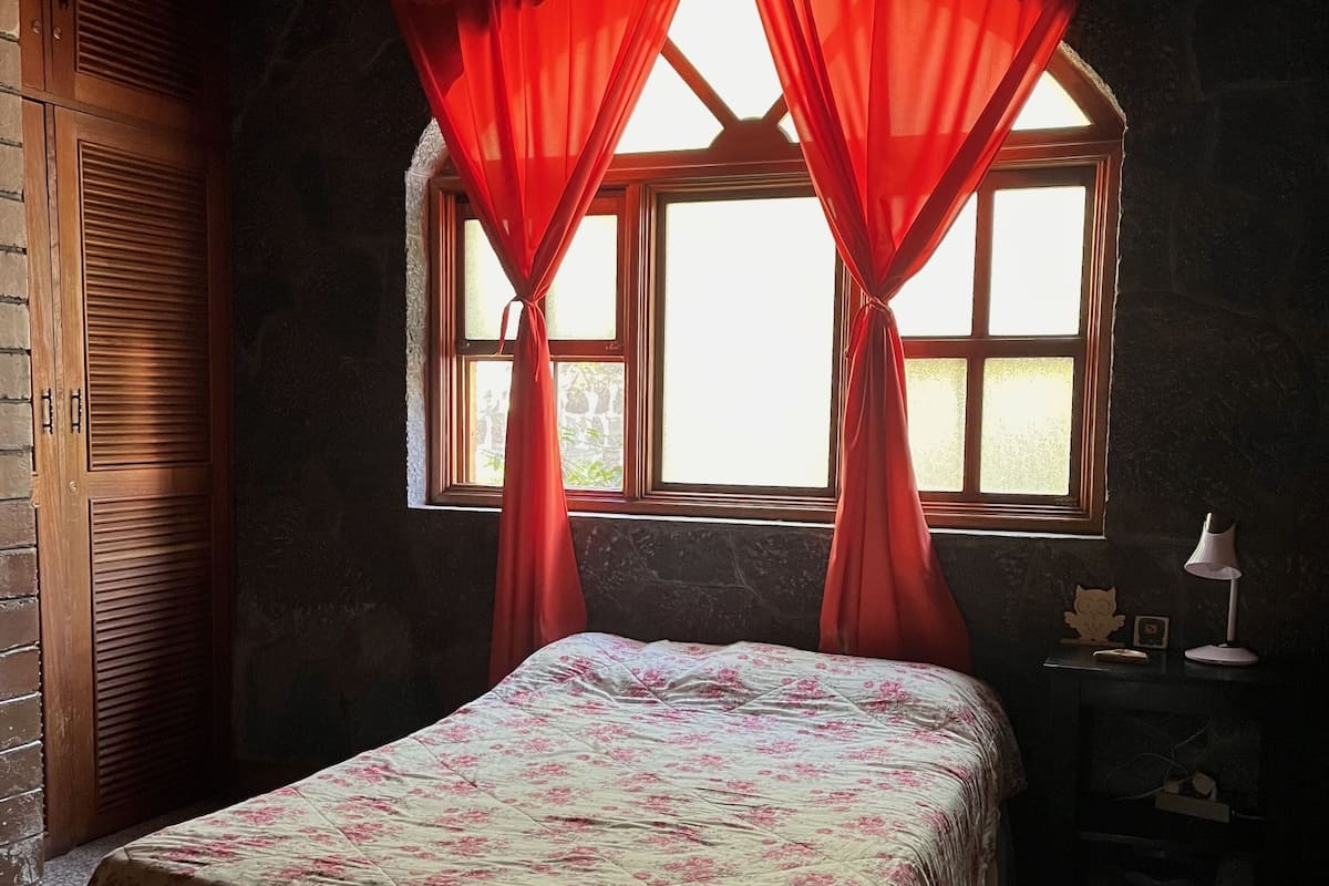 Un dormitorio con cama, ventana con cortinas, mesita de noche y pared con textura.