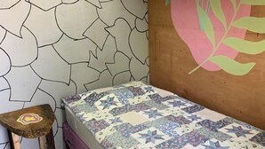 A bedroom with a patterned wall, a bed with a floral quilt, and a small wooden stool. - Casa Qatzij - Guest House (San Lucas Toliman)
