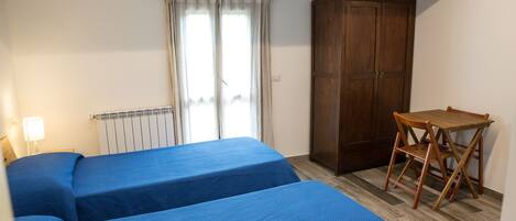 A room with two beds, a wooden desk, a chair, a radiator, and a wardrobe.
