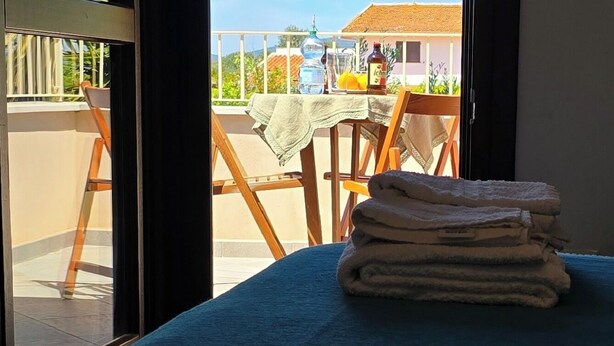 A room with a bed, a window with a view of a balcony, and a table with a tablecloth and bottles. - Alghero in Bicicletta (Alghero)