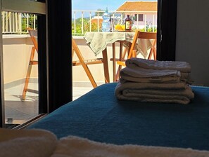A room with a bed, a window with a view of a balcony, and a table with a tablecloth and bottles. - Alghero in Bicicletta (Alghero)