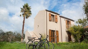 A two-story building with a balcony, a bicycle parked in front, and a palm tree nearby. - Alghero in Bicicletta (Alghero)