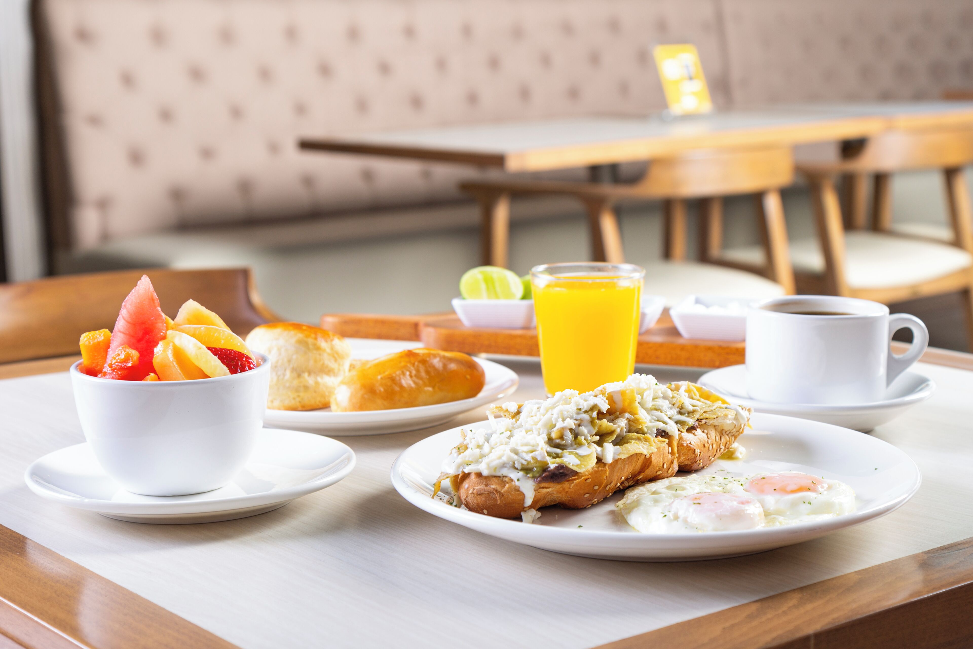 Una escena de desayuno con un bol de fruta, un croissant, una tortilla y café sobre una mesa.