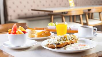 Una escena de desayuno con un bol de fruta, un croissant, una tortilla y café sobre una mesa.