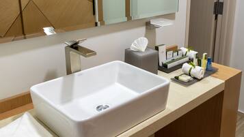 Un baño moderno con lavamanos blanco, espejo y artículos de tocador en la encimera.