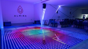 Une salle moderne dotée d’un grand écran LED au sol, d’un logo sur le mur et d’un espace repas avec des tables et des chaises.