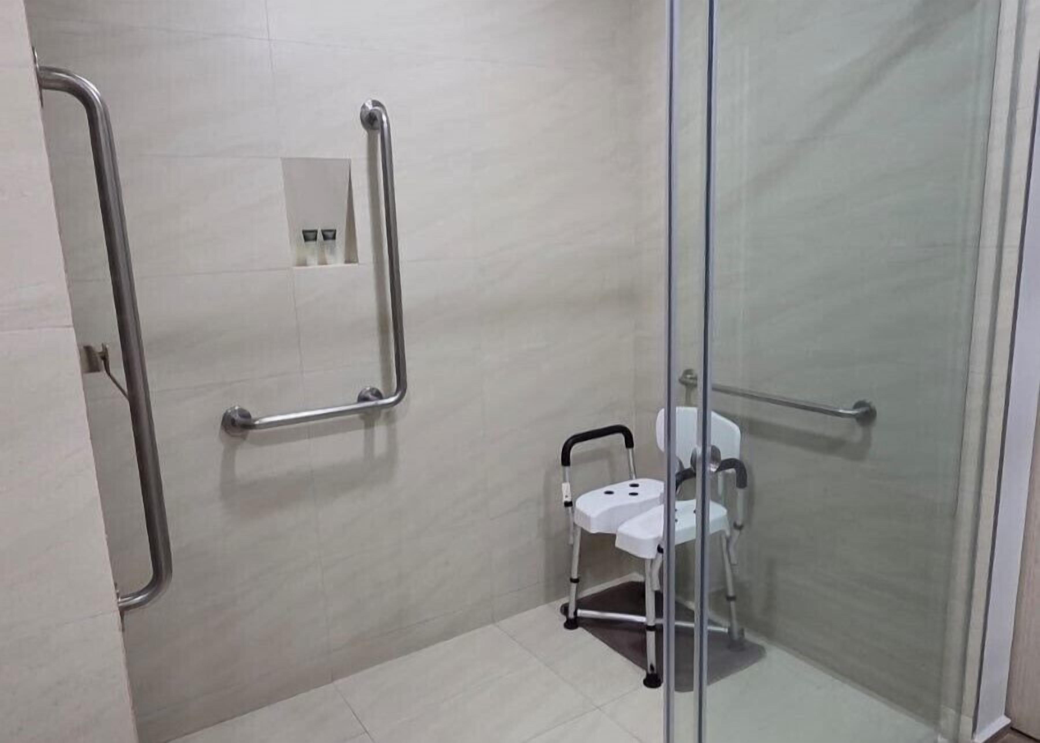 A bathroom with a glass shower enclosure, a white toilet, and a wheelchair-accessible bench.