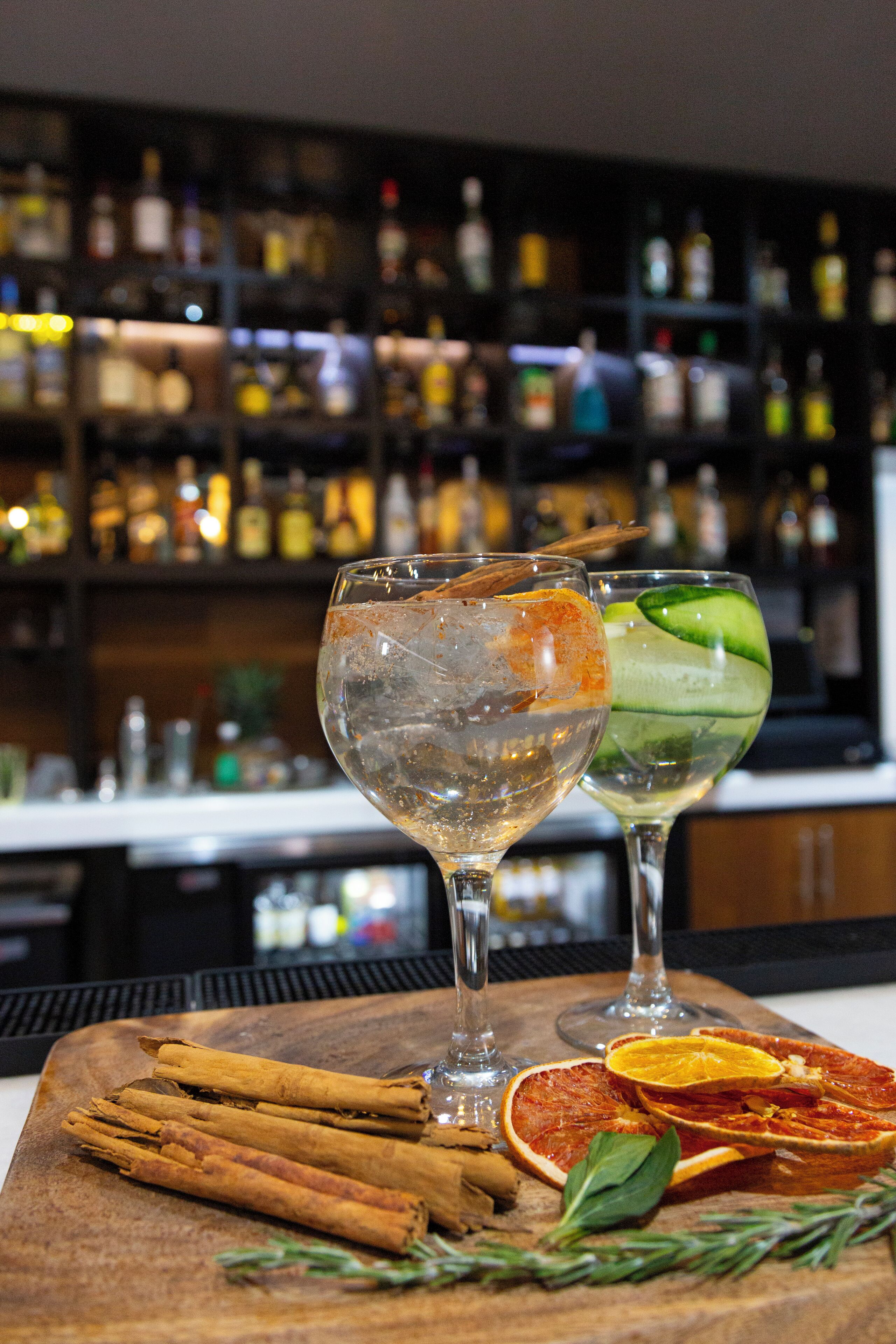 Two glasses of cocktails on a wooden board with cinnamon sticks and dried citrus slices.