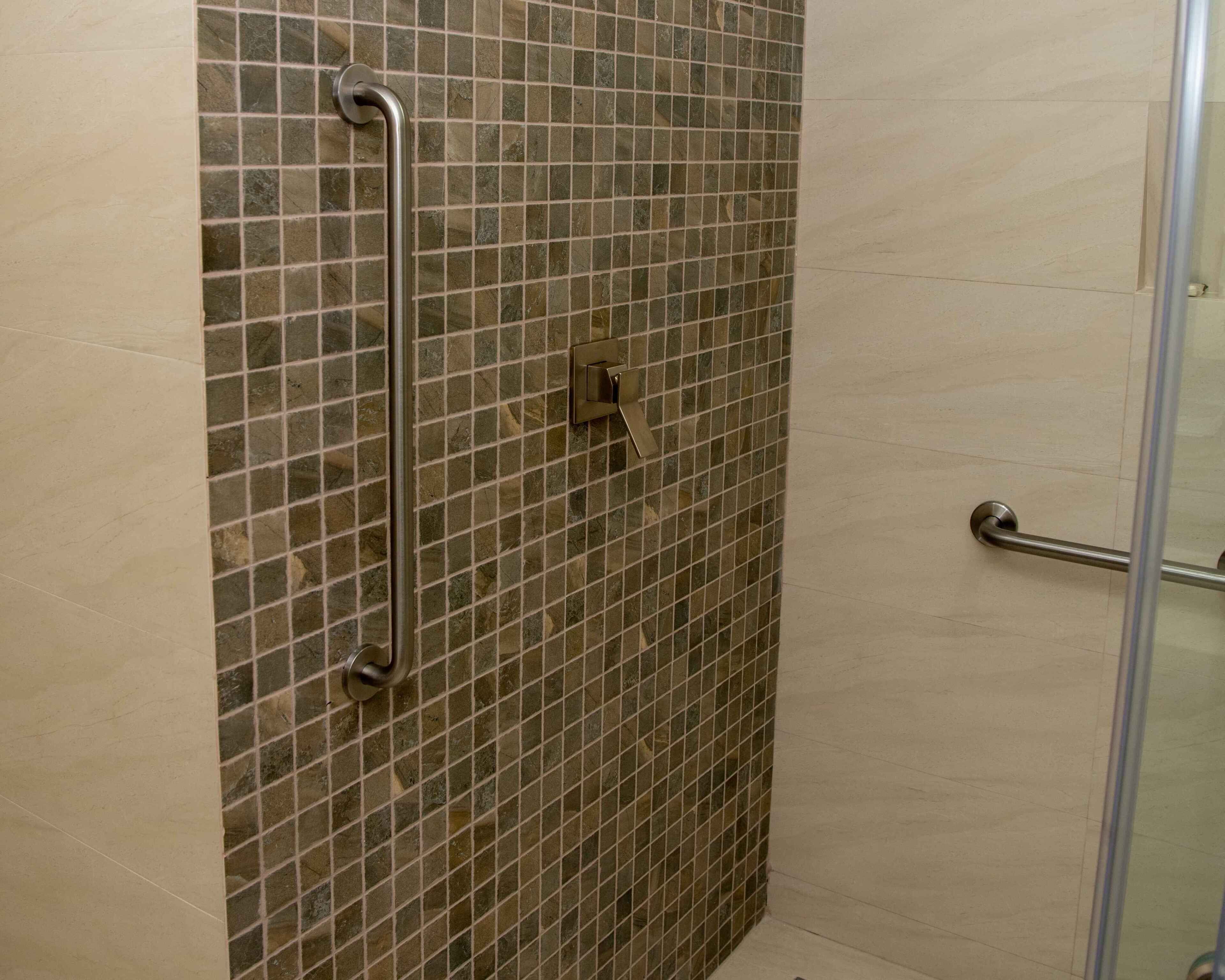 A shower area with a tiled wall, a glass door, and a handrail.