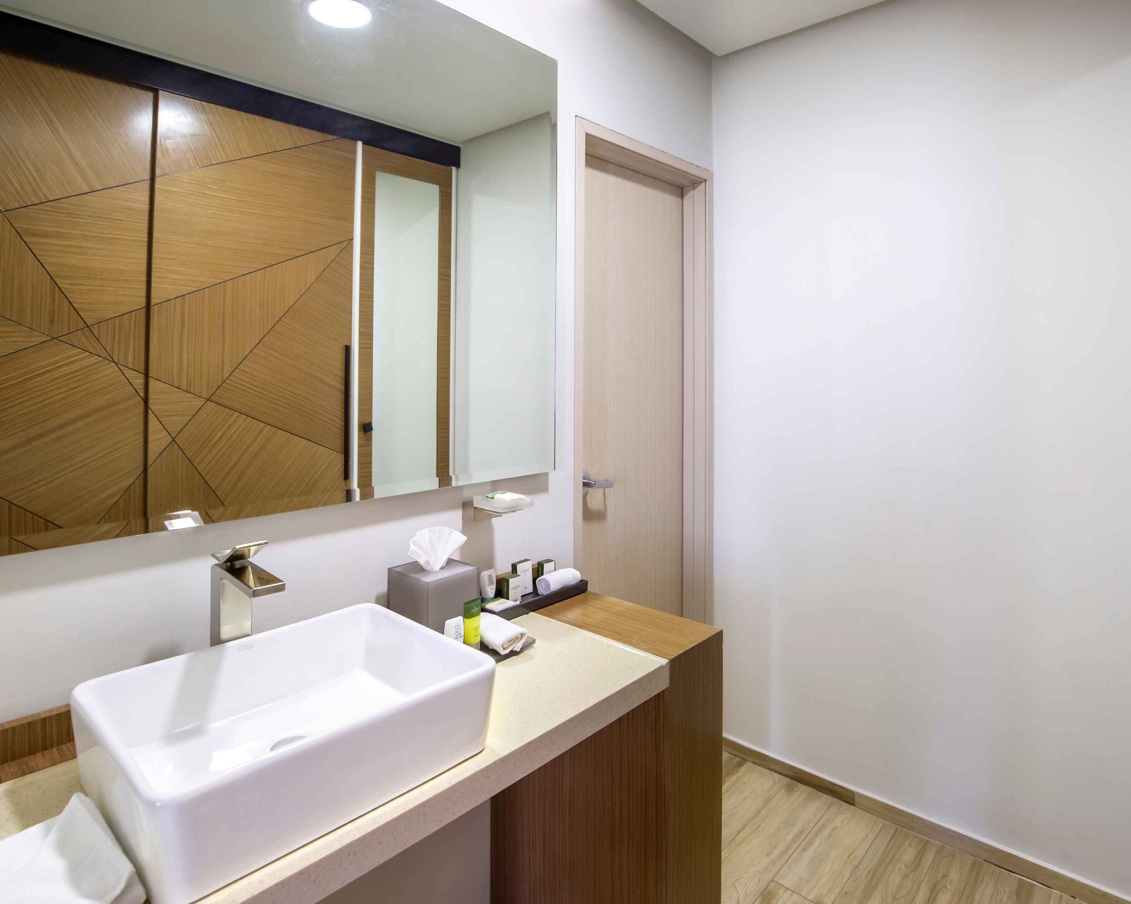 Un baño moderno con un espejo grande, un lavabo blanco y un mueble de tocador de madera.