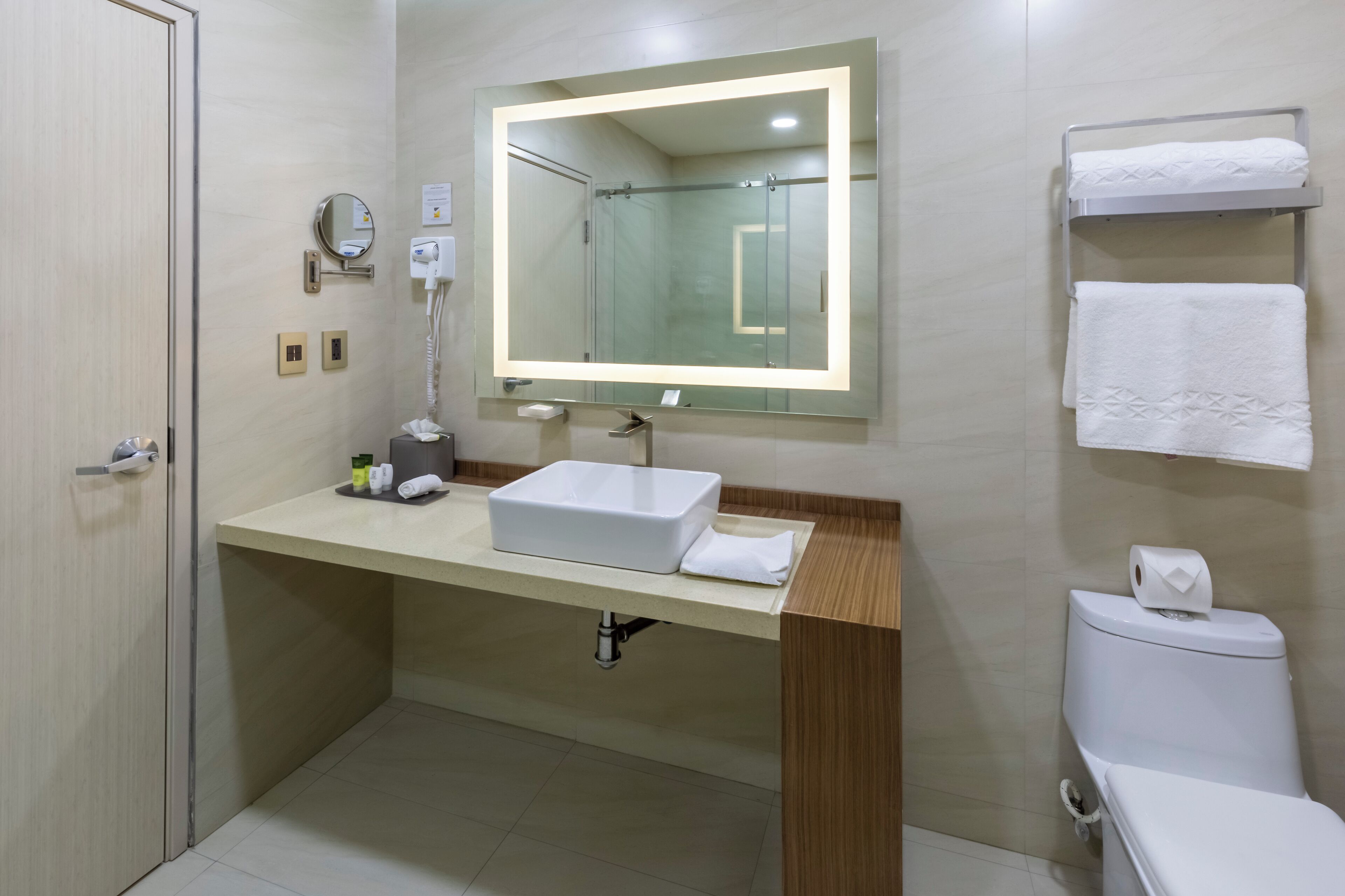 A modern bathroom with a large mirror, a white sink, a towel rack, and a toilet.