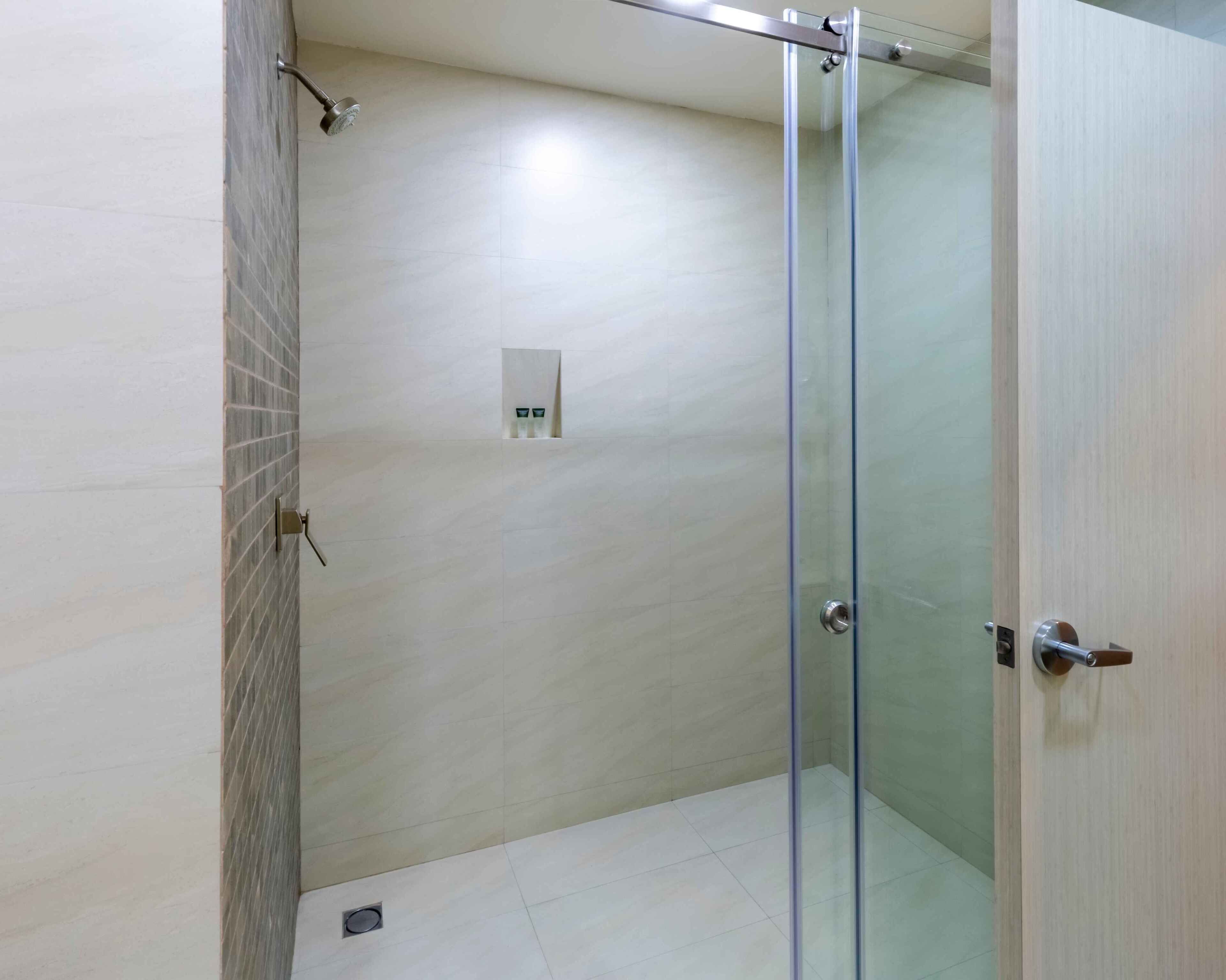 A modern bathroom with a glass shower enclosure, a tiled floor, and a wall-mounted light fixture.
